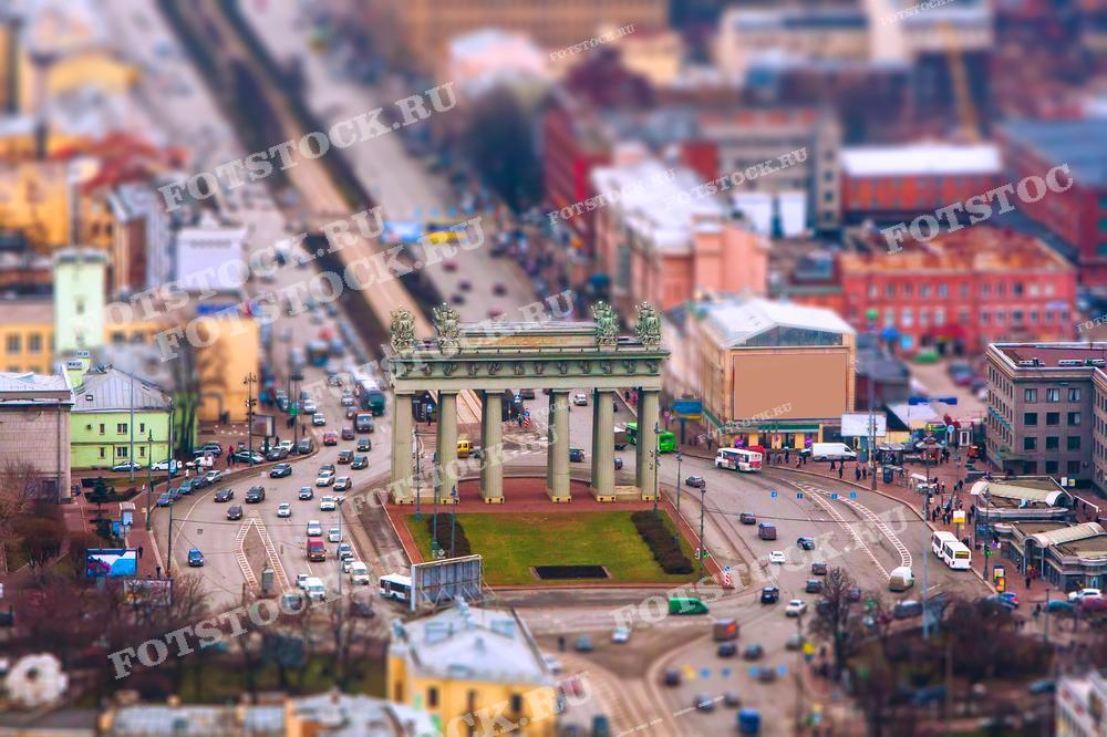 На фотографии изображены Московские триумфальные ворота в Санкт-Петербурге, снятые с высоты. Вид сверху позволяет увидеть прилегающую дорожную развязку и окружающие здания. Фото идеально подходит для использования в туристических буклетах, образовательных материалах и иллюстрациях в СМИ.